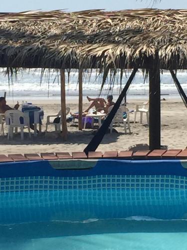 a swimming pool with a straw umbrella and a beach at Casa de las Olas Surf & Beach Club in Acapulco