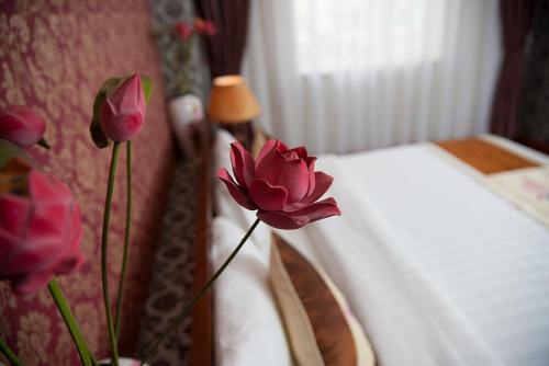 a vase of pink flowers next to a bed at First Eden Hotel - Hang Bun in Hanoi