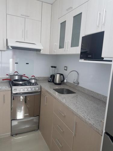 a kitchen with white cabinets and a stove and a sink at Nino´s Residence Departamentos VIP Amoblados in Tacna