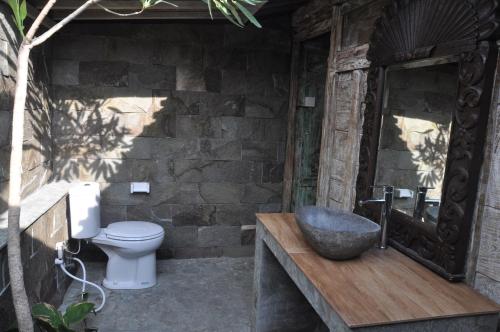 a bathroom with a toilet and a stone wall at Kubudiuma Villas Bali in Canggu