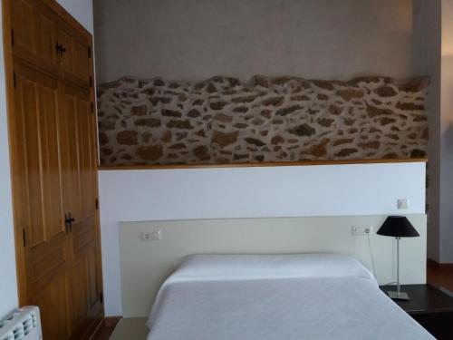 a bedroom with a white bed and a stone wall at Casa Rural La Antigua Fragua in Los Llanos de Tormes