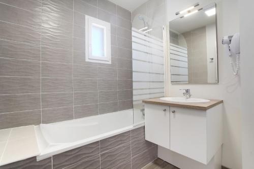 a bathroom with a sink and a tub and a mirror at Résidence Odalys Fleur de Sel in Aigues-Mortes