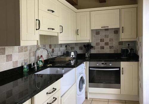 a kitchen with white cabinets and a sink and a dishwasher at Val Rive - Le Pintadeau Cottage - Dinan in Dinan