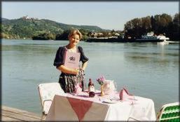a woman standing in front of a table next to a lake at Fischwirtshaus Landmotel Die Donaurast in Persenbeug-Gottsdorf