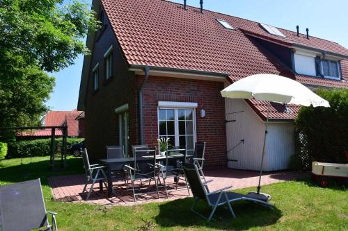 patio con tavolo, sedie e ombrellone di Ferienhaus Carolinenwind a Carolinensiel
