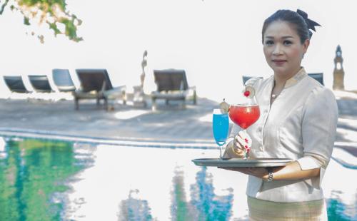 a woman holding a tray with two cocktails on it near a pool at Rajapruek Samui Resort - SHA Plus in Lipa Noi