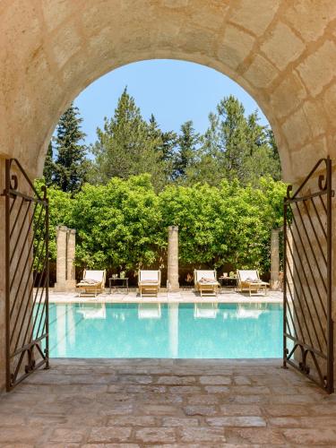 an archway leading to a swimming pool with chairs and trees at Masseria Marzalossa in Fasano