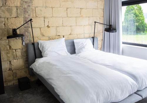 a bed with white sheets in a room with a brick wall at K-Kanne in Kanne