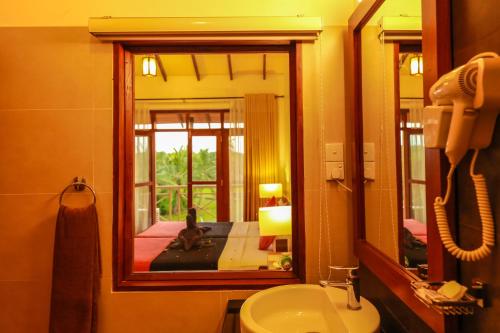 a bathroom with a mirror and a cat sitting on a sink at Pelwehera Village Resort in Dambulla