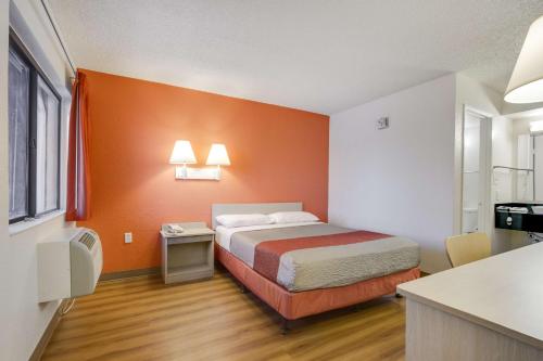 a small room with a bed and an orange wall at Motel 6-Tempe, AZ - Broadway - ASU in Tempe