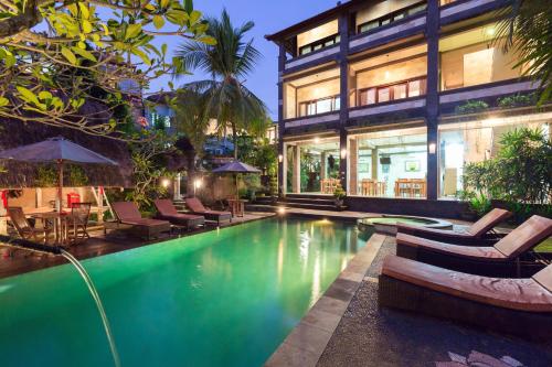 a pool in front of a building with chairs and a house at Wenara Bali Bungalows in Ubud