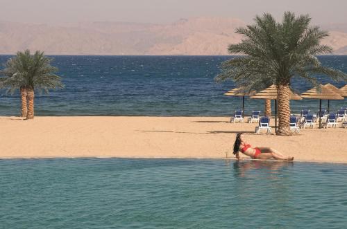 a woman laying in the water on the beach at Mövenpick Resort & Spa Tala Bay Aqaba in Aqaba