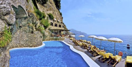 a swimming pool next to the ocean with chairs and umbrellas at Hotel Santa Caterina in Amalfi