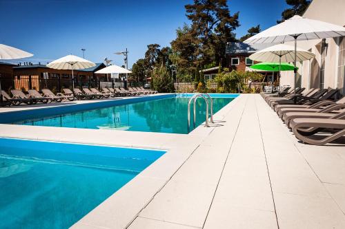 a swimming pool with chairs and umbrellas next to a building at Alcest Niechorze in Niechorze