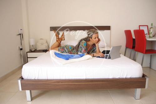 Eine Frau, die mit einem Laptop auf einem Bett liegt. in der Unterkunft Peyia Pearl in Peyia