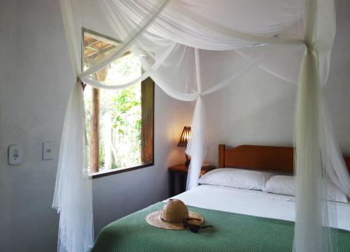 a bedroom with a bed with a hat and a window at Canto do Sabiá Caraíva in Caraíva