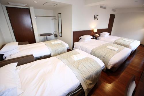 three beds in a hotel room with white sheets at Sutton Hotel Hakata City in Fukuoka