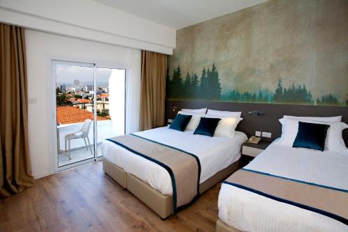 リマソールにあるPefkos City Hotelのベッド2台とバルコニーが備わるホテルルームです。