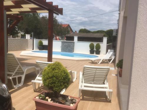 une terrasse avec des chaises blanches et une piscine dans l'établissement Villa Vinko, à Rogoznica