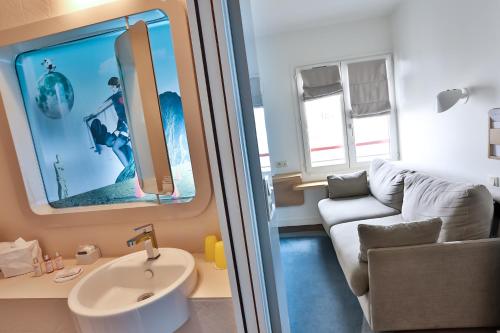 a bathroom with a sink and a couch in a room at Hôtel Le Marcel Paris Gare de l'Est in Paris