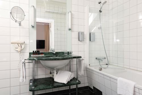 a white bathroom with a sink and a bath tub at Elite Stadshotellet Växjö in Växjö