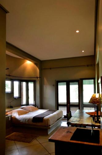 a bedroom with a bed and a desk and windows at Tingala Lodge - Bed in the Bush in Phalaborwa