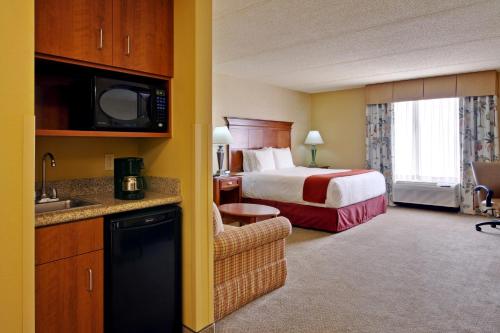 Holiday Inn Express & Suites Bloomington, an IHG Hotel في بلومنغتون: غرفة الفندق بسرير كنج ومطبخ