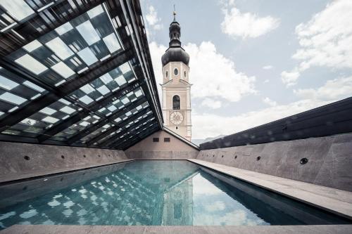 a building with a clock tower and a swimming pool at Hotel Lamm in Castelrotto