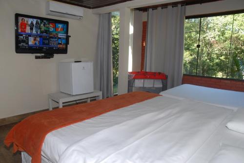 a bedroom with a large bed with a tv on the wall at Pousada Mirante do Penedo in Penedo