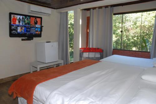 a bedroom with a large bed with a tv on the wall at Pousada Mirante do Penedo in Penedo