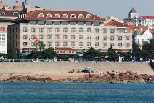 a large white building with a beach in front of the water at Qingdao Oceanwide Elite Hotel in Qingdao