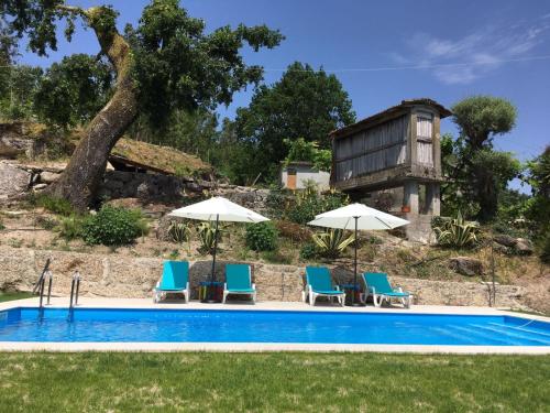 a pool with chairs and umbrellas and a house at Casa Cima de Vila in Vieira do Minho