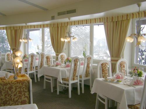 un comedor con mesas y sillas blancas y ventanas en Alpenhotel Kronprinz, en Berchtesgaden