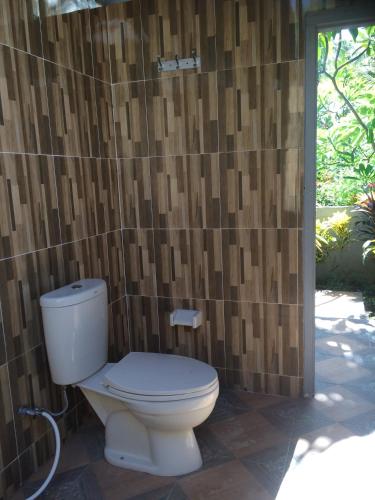 a bathroom with a toilet and a wall with wood at Bali Segara Lestari Oceanfront Villas in Tejakula