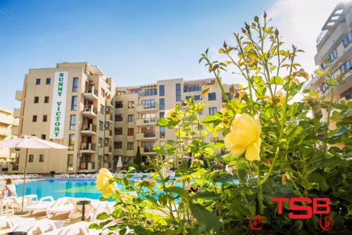a pool with some yellow flowers and some buildings at TSB Sunny Victory in Sunny Beach