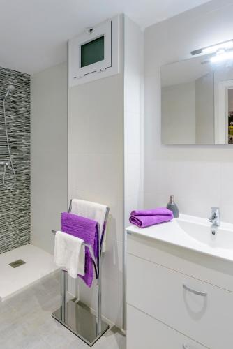 a white bathroom with a sink and purple towels at NS Apartaments in Tossa de Mar