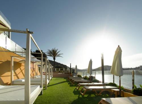 a row of lounge chairs and umbrellas next to the water at Palladium Hotel Cala Llonga - Adults Only in Cala Llonga