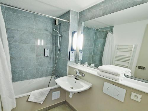 een badkamer met een wastafel, een bad en een spiegel bij Kyriad Cambrai in Cambrai