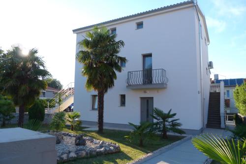 a white house with a balcony and palm trees at Apartments Monja & Dadi in Vantačići