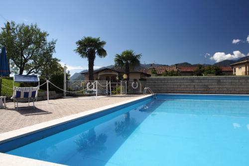 a blue swimming pool with a chair and palm trees at Hotel Garni Bel Sito in Tremosine Sul Garda
