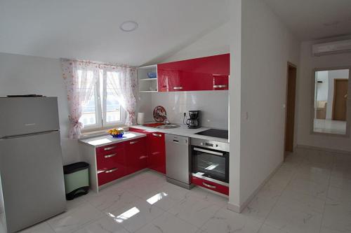 a small kitchen with red cabinets and a refrigerator at Apartment Carlitos in Karlobag