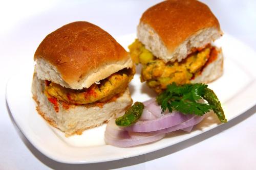 a white plate with a sandwich and some vegetables at Hotel Pearl in Navi Mumbai