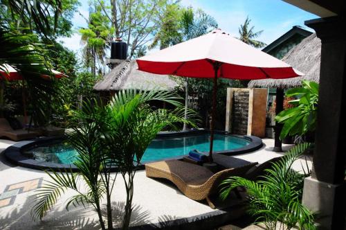 a swimming pool with a red umbrella and chairs and a table and an umbrella at Gili Flush Harmony in Gili Trawangan