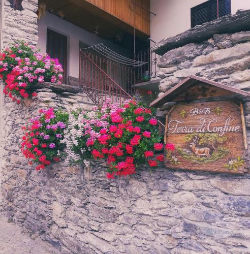 un cartello sul lato di un muro di pietra con fiori di B&B Terra di confine a Venalzio