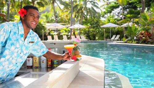 a man holding a drink at a bar next to a pool at Castaway Island, Fiji in Castaway Island