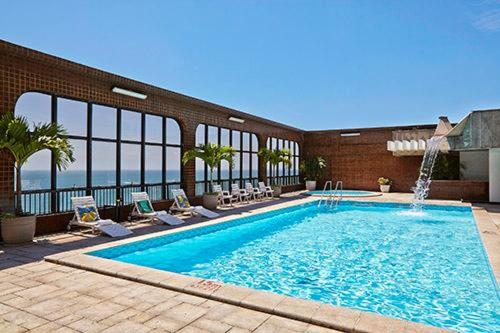 a large swimming pool with chairs and a building at Pasargada Praia da Costa in Vila Velha