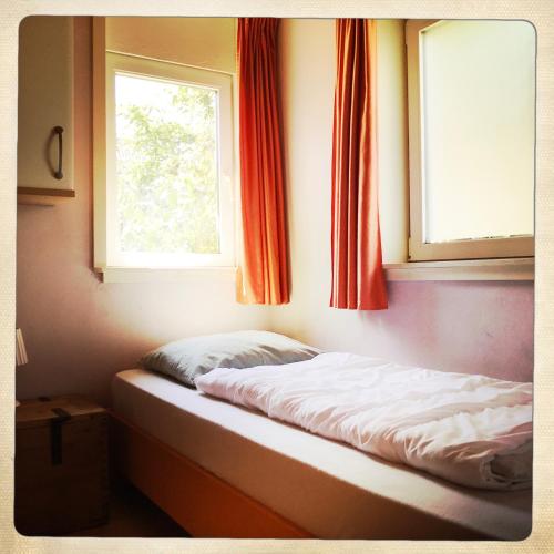 a bed sitting in a room with two windows at De Munnik in Camperduin