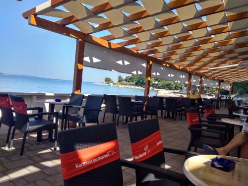 ein Restaurant mit Blick auf den Strand mit Tischen und Stühlen in der Unterkunft Barka Zadar in Zadar