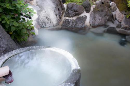 a body of water with a rock wall and a tub of water at Kurokawa Onsen Ryokan Ichinoi in Minamioguni