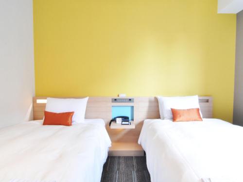two beds in a room with a yellow wall at Sotetsu Grand Fresa Osaka-Namba in Osaka